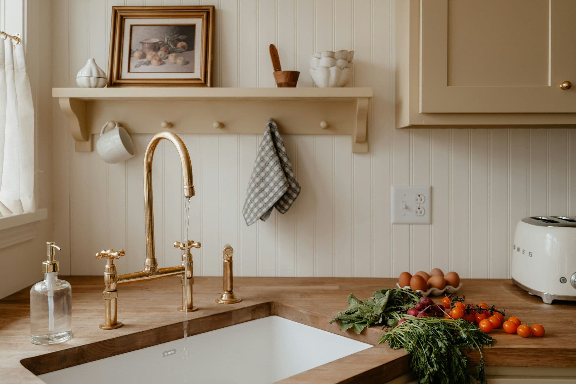 A butcher-block worktop and white sink under an aged-brass bridge tap, with a peg rail and tea towel behind