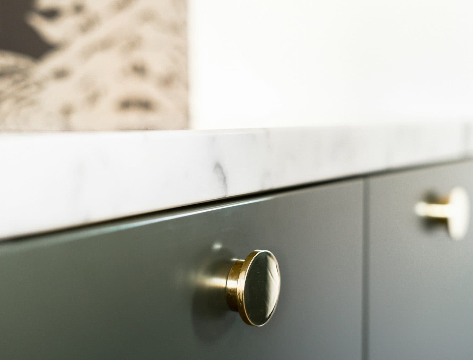 Close-up of a brass knob on a green drawer front beneath a stone worktop edge
