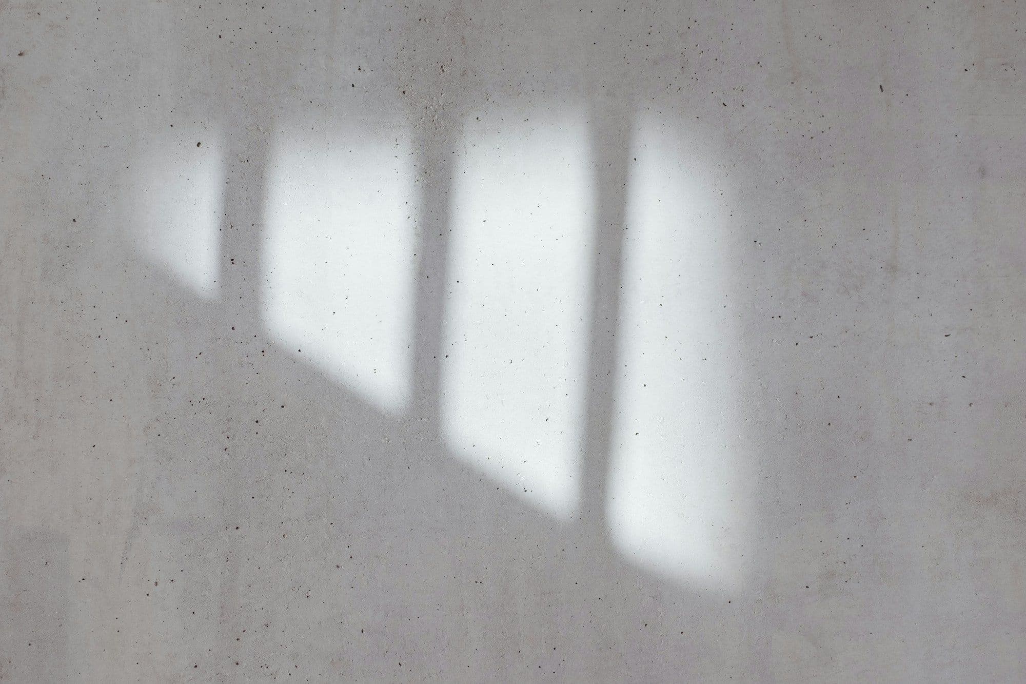 A dead-flat pale plaster wall with window light falling across it