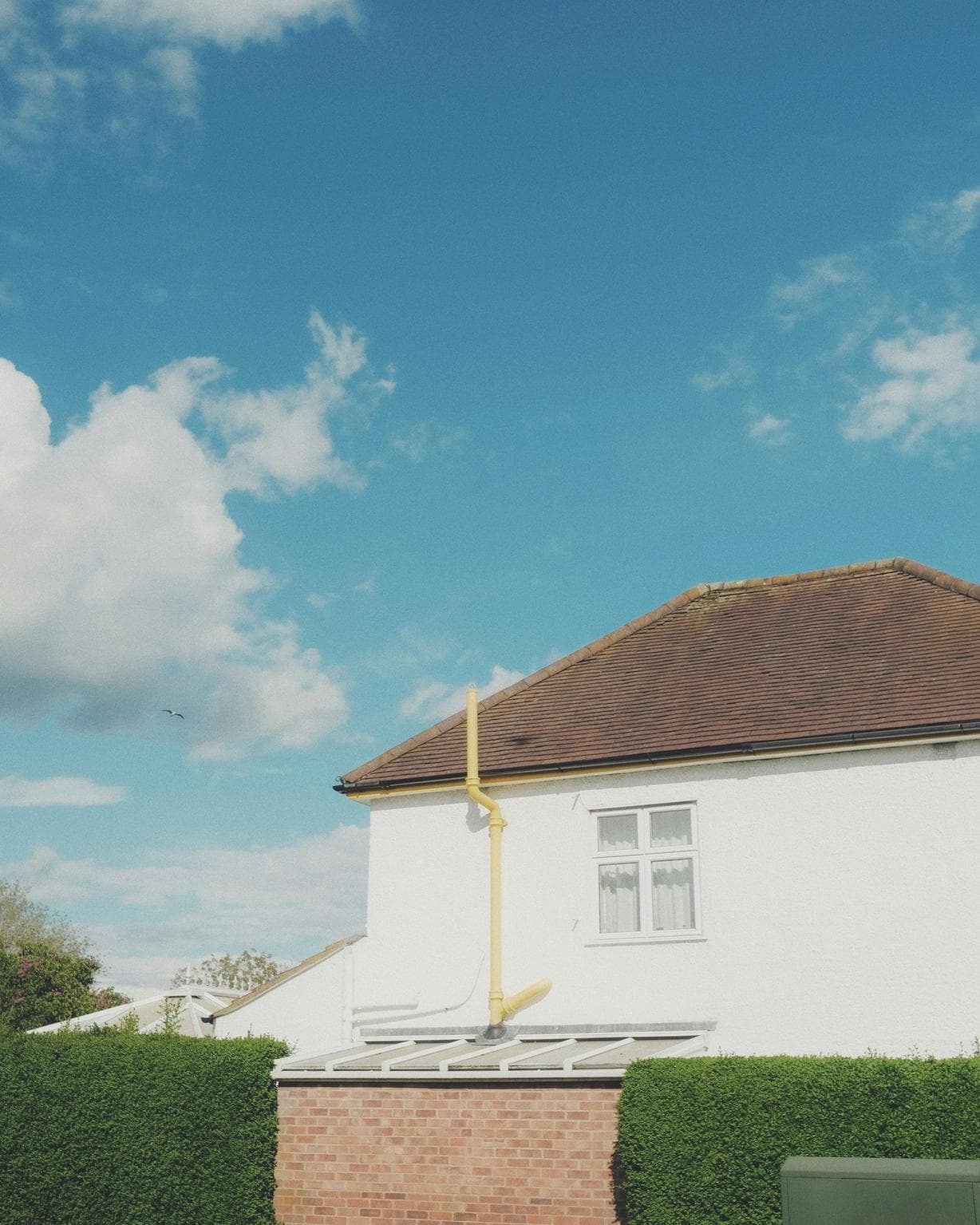 A freshly rendered white house wall with a clay-tiled roof against a blue sky