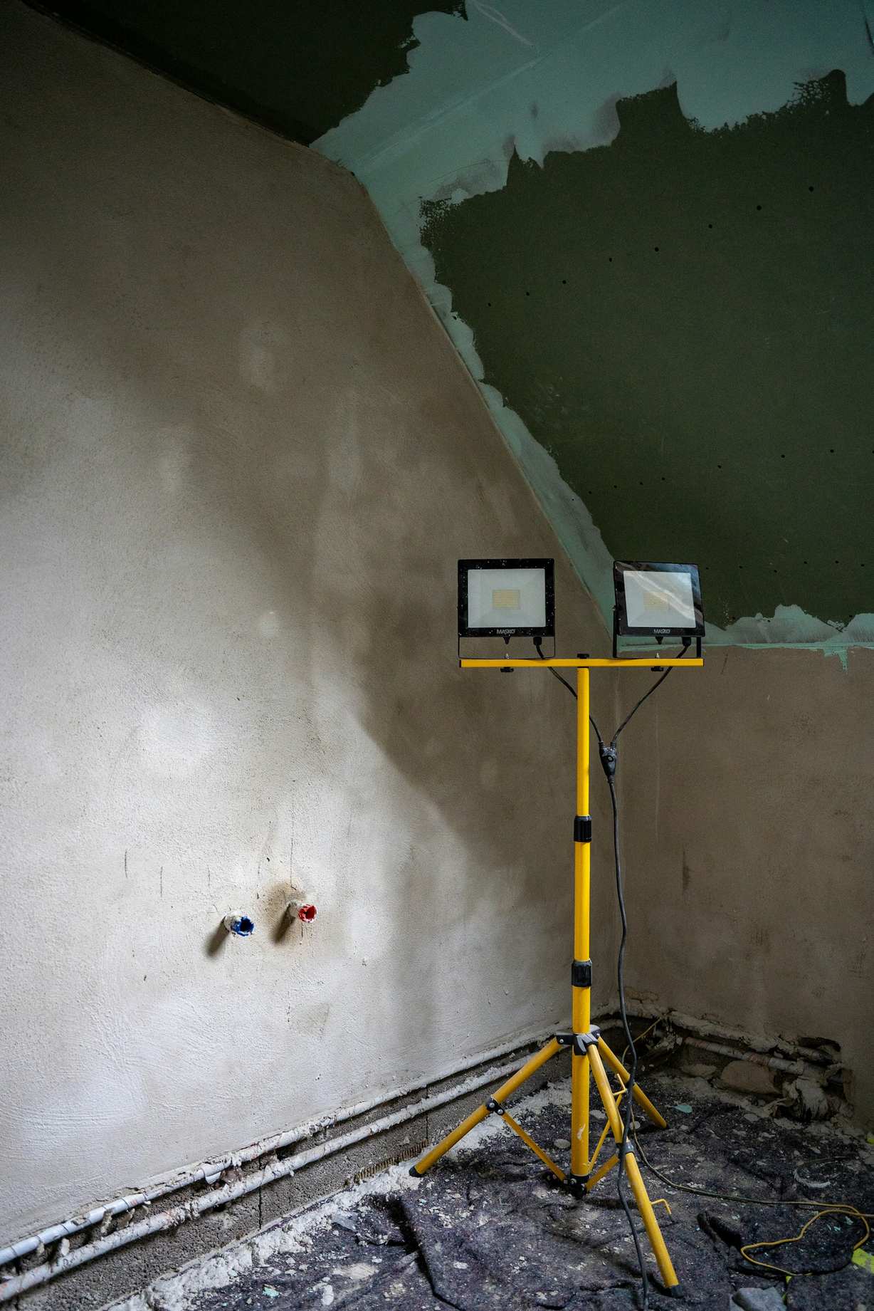 A room mid-renovation with fresh grey plaster on the walls and a site light on a tripod