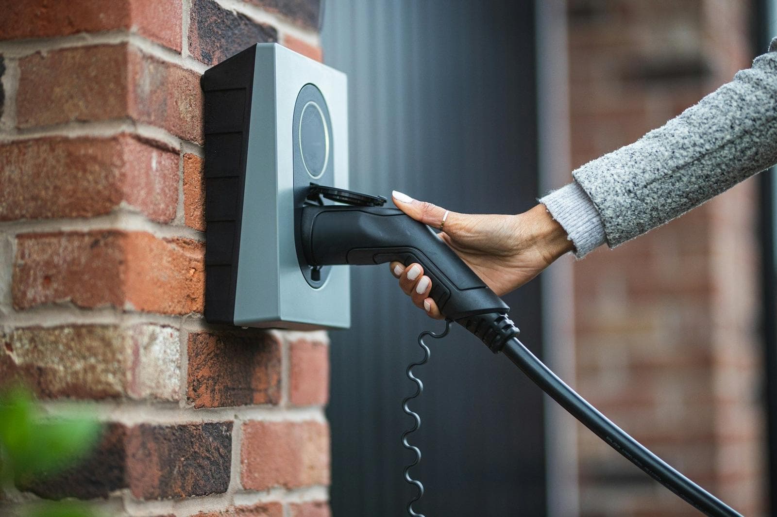 A hand plugging an EV charging cable into a wall-mounted charger